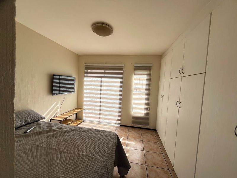 A bedroom featuring tiled flooring, built-in cupboards for storage, and roller blinds on the windows, providing a functional and well-lit living space.