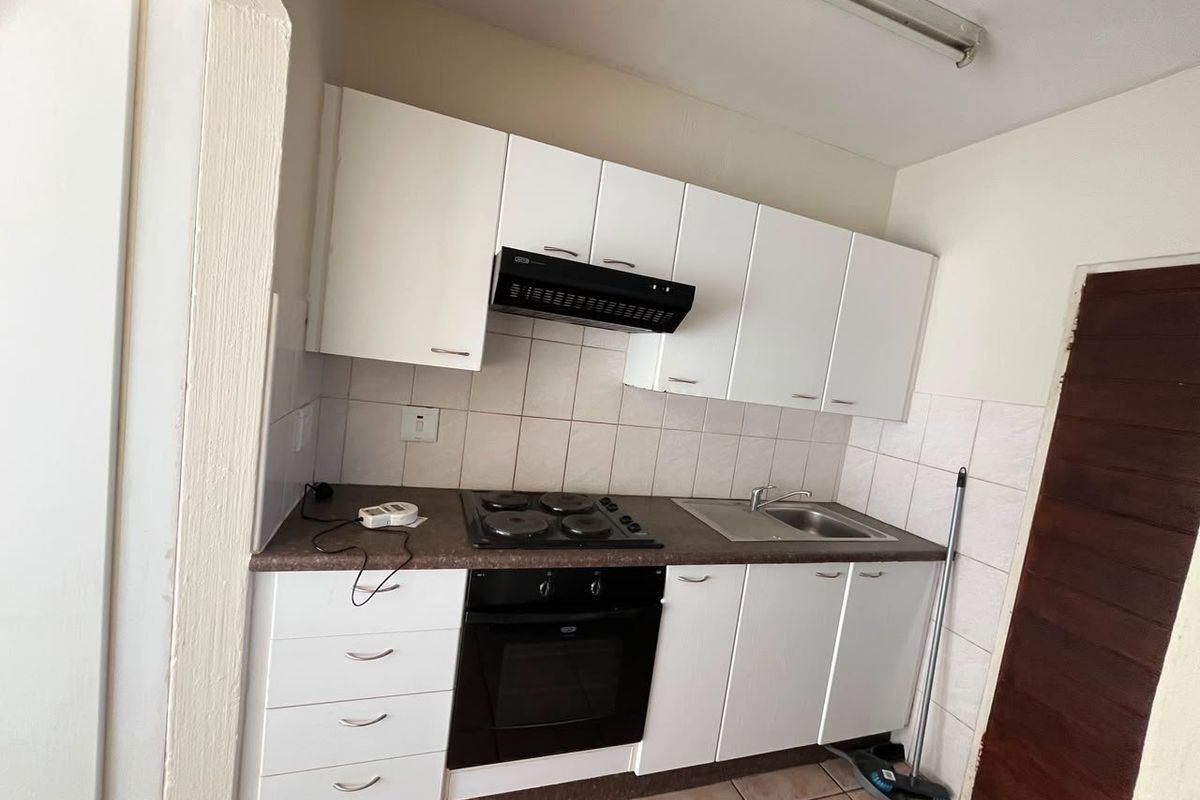 Compact kitchen featuring white cabinetry, built-in oven and hob, stainless steel sink, and tiled backsplash.