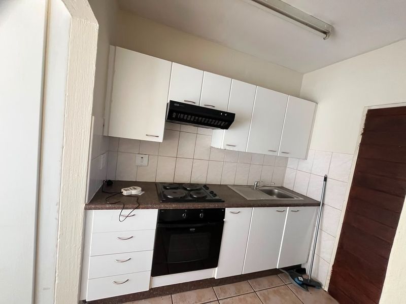 Compact kitchen featuring white cabinetry, built-in oven and hob, stainless steel sink, and tiled backsplash.