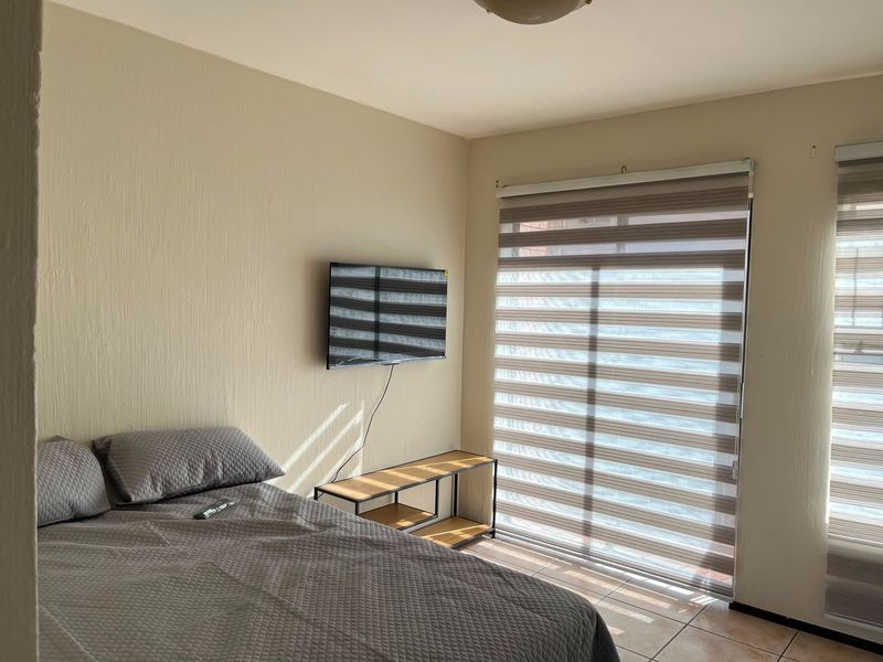 A well-lit bedroom featuring neutral wall finishes, tiled flooring, and modern dual-layer roller blinds providing adjustable natural light.