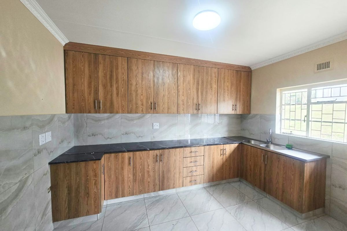 A clean, modern kitchen featuring wood-look cabinetry, dark stone countertops, tiled backsplash, and tiled flooring, offering a functional and well-maintained workspace.