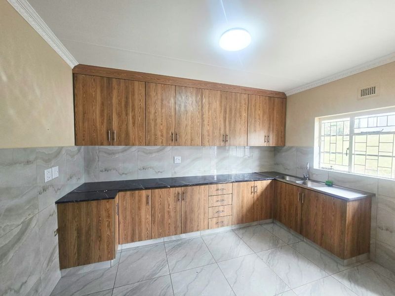 A clean, modern kitchen featuring wood-look cabinetry, dark stone countertops, tiled backsplash, and tiled flooring, offering a functional and well-maintained workspace.