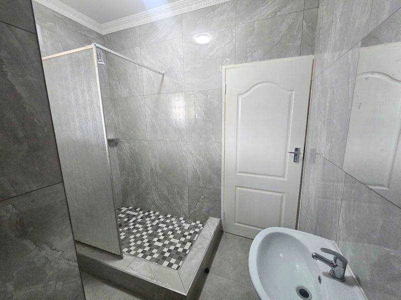 A modern bathroom featuring grey marble-effect wall tiles, a walk-in shower with a glass screen, and a pedestal basin.