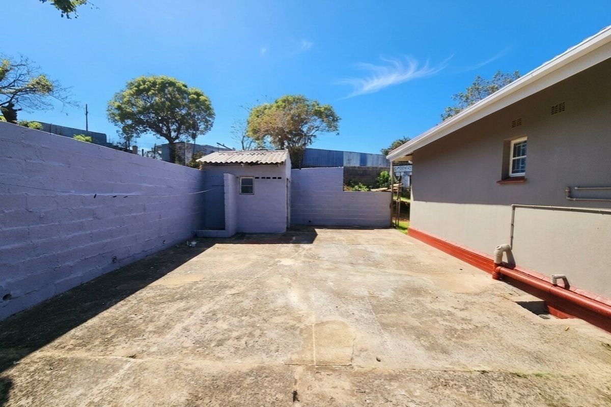 A rear exterior view of the property featuring a paved courtyard area, boundary walls, and a small outbuilding.
