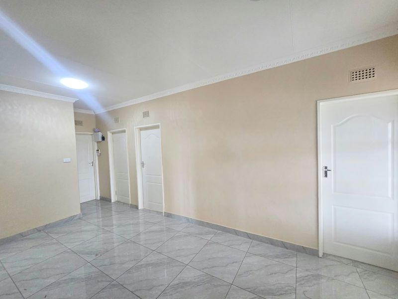 A spacious, empty hallway featuring neutral wall tones, modern grey tiled flooring, and multiple internal doors with decorative cornicing.