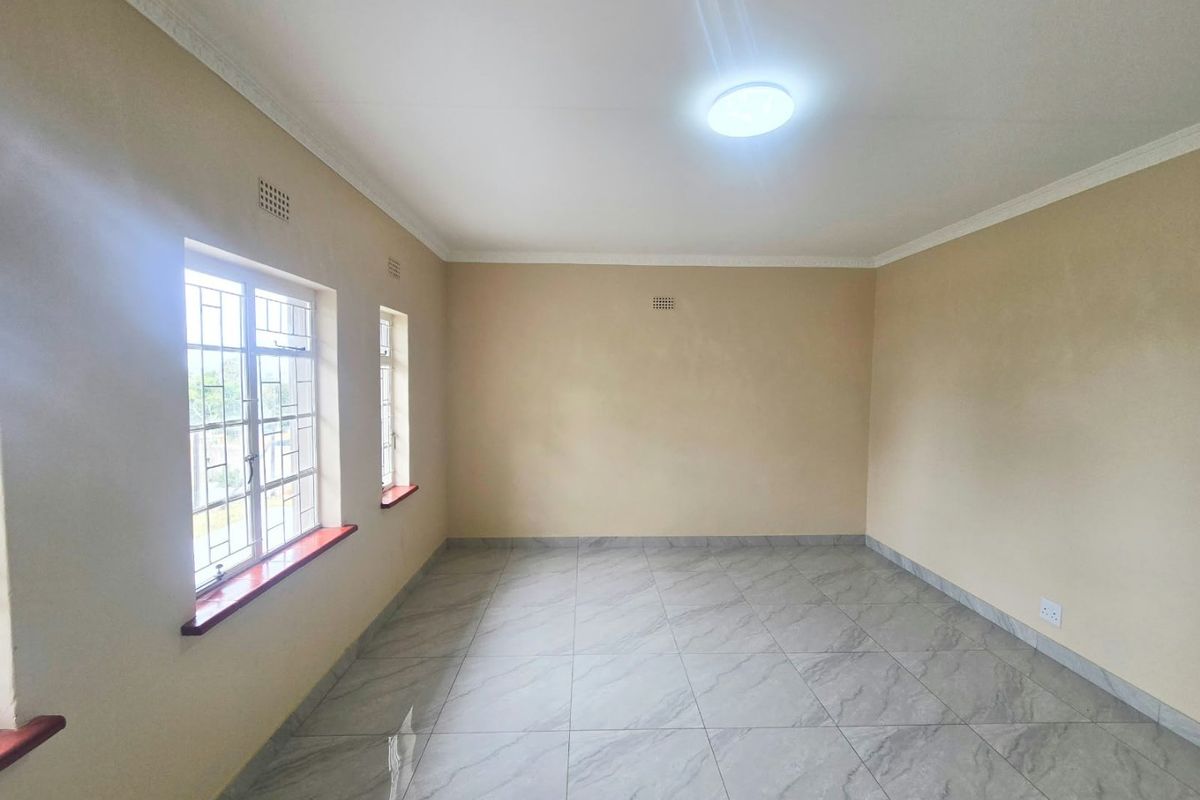 A bright, empty living room featuring neutral walls, modern grey tiled flooring, and windows fitted with security bars.