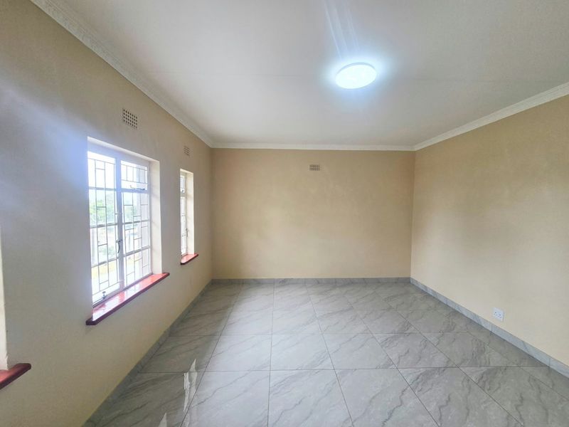 A bright, empty living room featuring neutral walls, modern grey tiled flooring, and windows fitted with security bars.