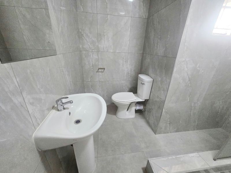 Modern bathroom featuring large-format grey porcelain wall and floor tiles, a white pedestal washbasin, and a standard toilet.