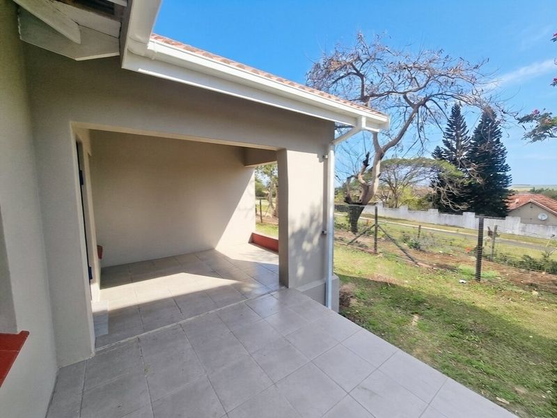A covered outdoor patio area featuring tiled flooring, overlooking the garden and surrounding property grounds.