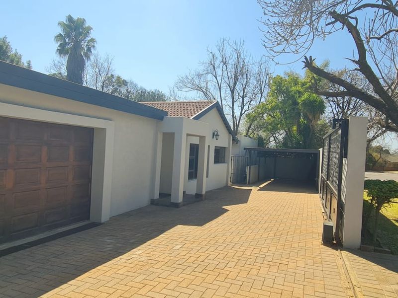 Front exterior view featuring a paved driveway, a garage, and a covered carport area with established garden surroundings.