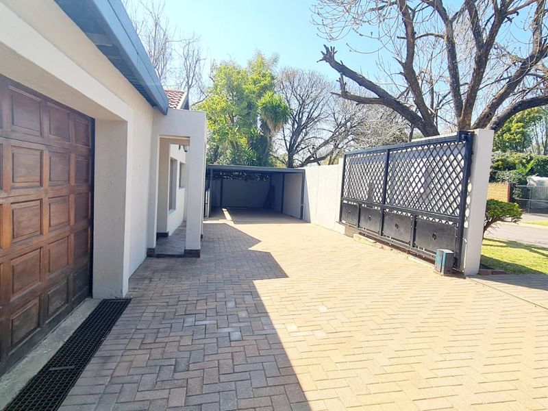 Front exterior view featuring a paved driveway, wooden garage door, sliding security gate, and a covered carport area.