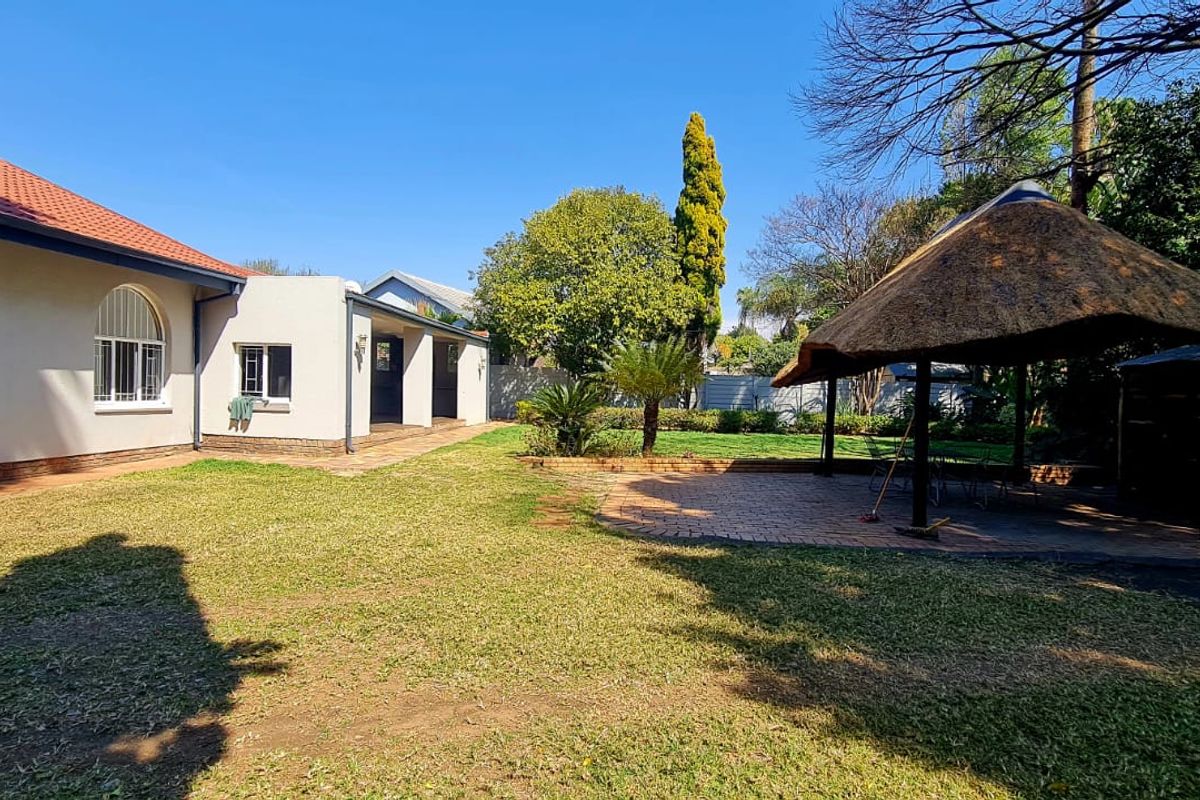 Spacious rear garden featuring a paved patio area, a traditional thatched lapa, and well-maintained lawn space adjacent to the main house structure.