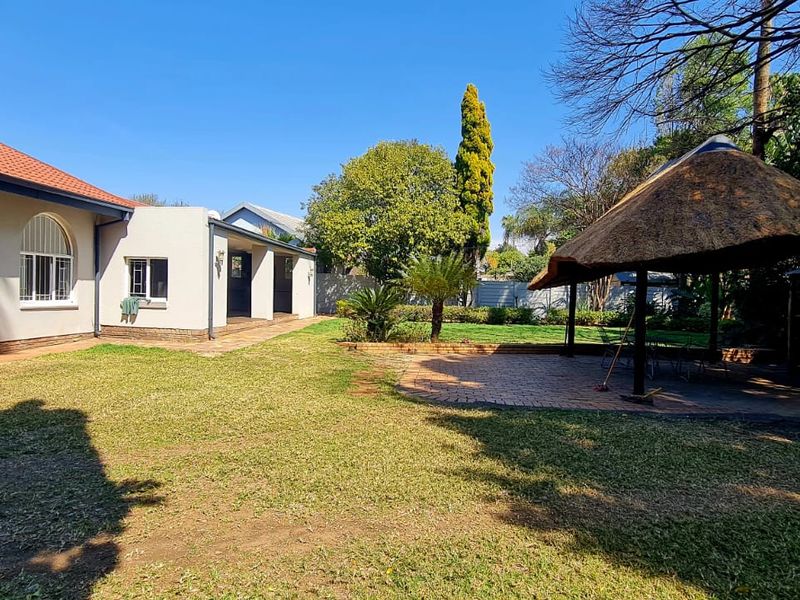 Spacious rear garden featuring a paved patio area, a traditional thatched lapa, and well-maintained lawn space adjacent to the main house structure.