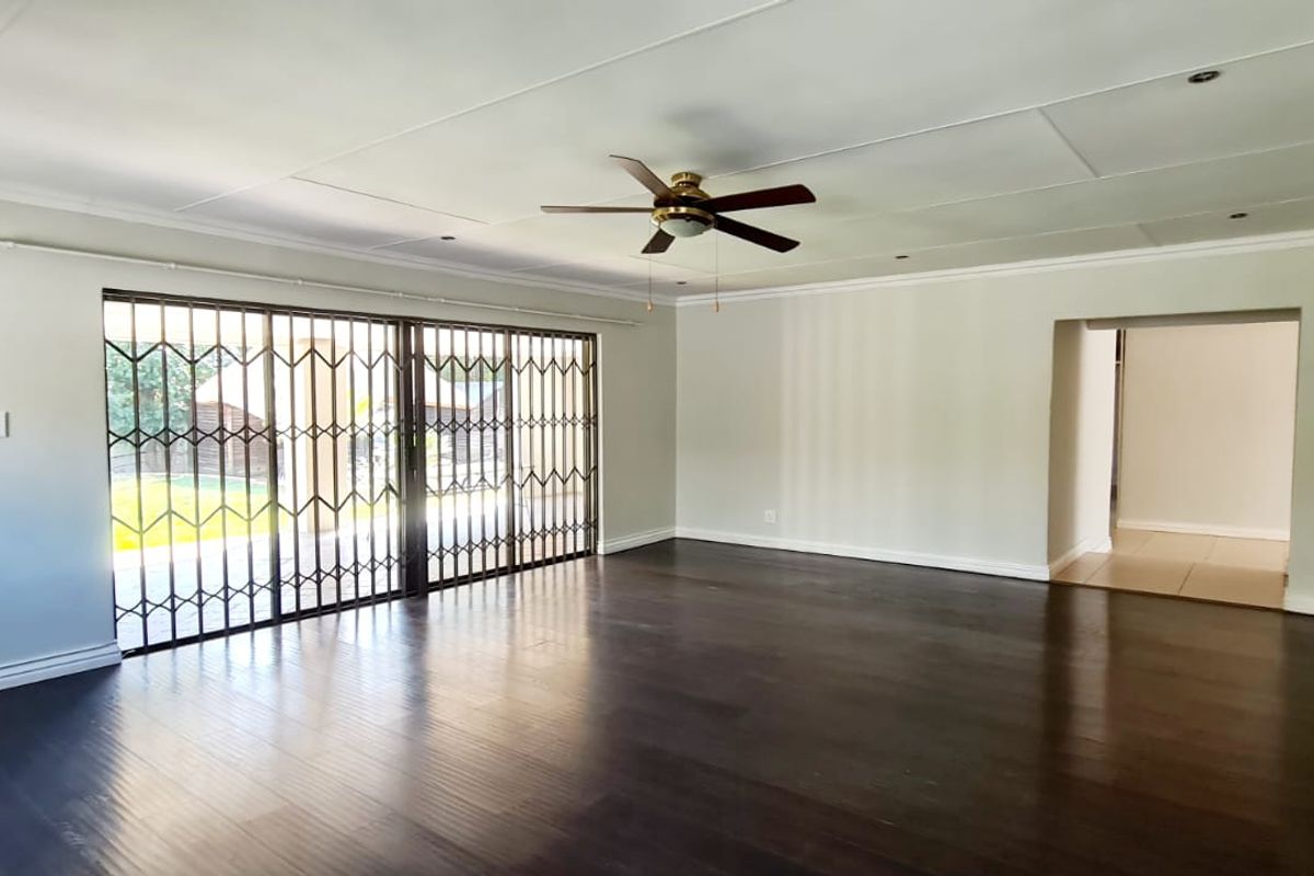 Spacious, light-filled living area featuring dark laminate flooring, a ceiling fan, and large sliding doors with security gates leading to the outdoor space.