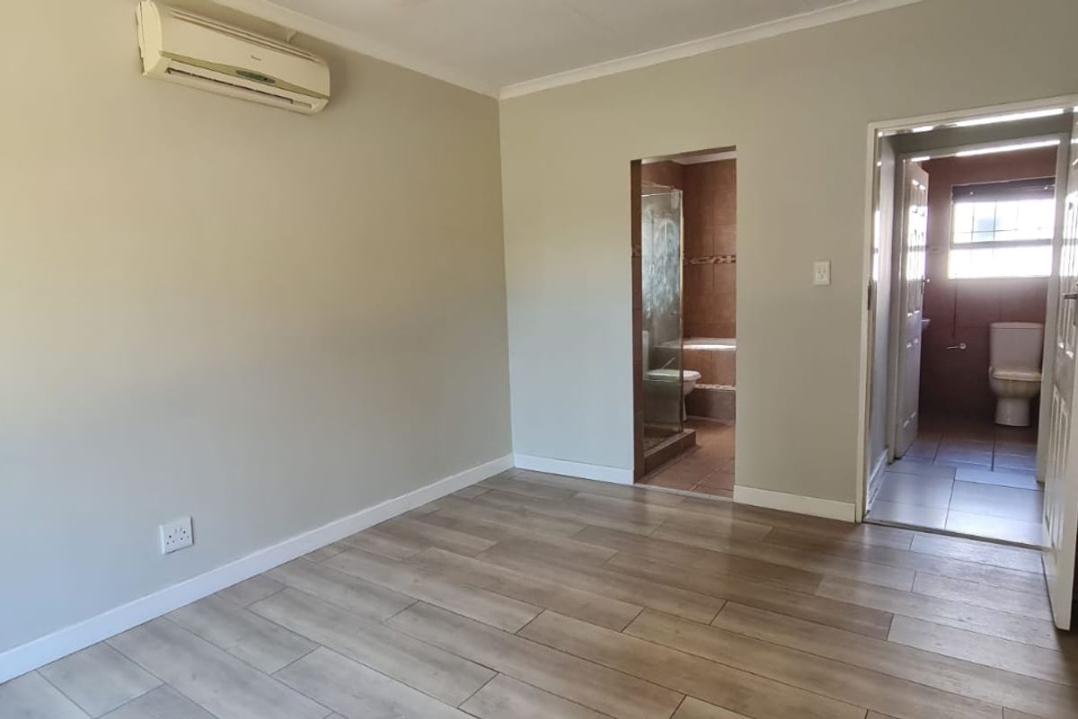 Spacious bedroom featuring wood-look tiled flooring, built-in cupboards, a wall-mounted air conditioning unit, and direct access to an en-suite bathroom.
