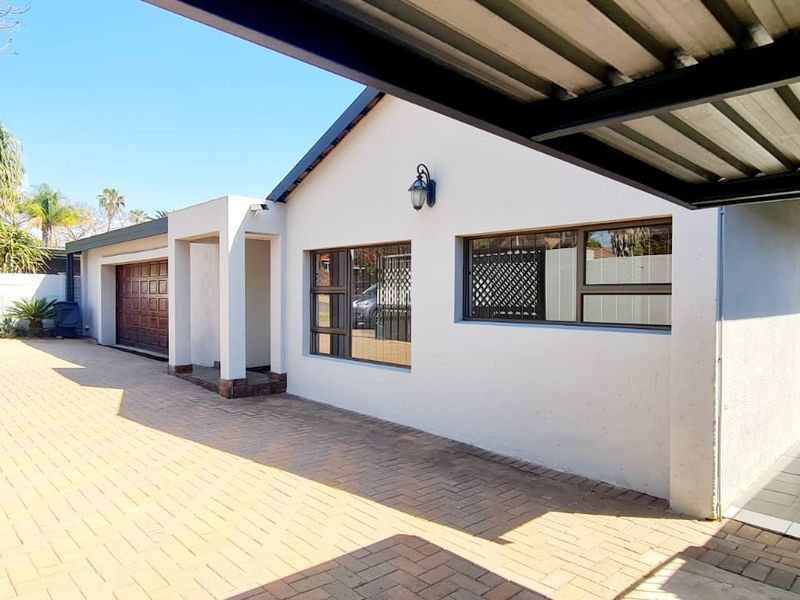 Front exterior view featuring a paved driveway, covered carport, and secure garage access with well-maintained white facade and aluminium window frames.
