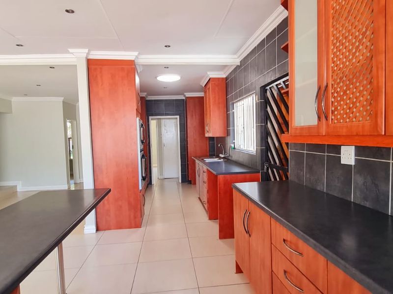 A spacious kitchen featuring warm-toned built-in cabinetry, dark countertops, tiled backsplash, and integrated double wall ovens, flowing into an open-plan living area.