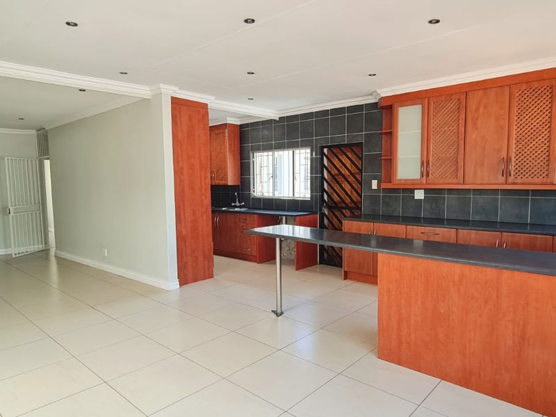Spacious open-plan living area featuring a functional kitchen with wooden cabinetry, a breakfast bar, and neutral tiled flooring throughout.