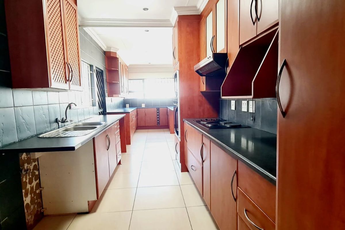 A galley-style kitchen featuring wooden cabinetry, dark countertops, a built-in hob, and tiled finishes, offering a functional layout with ample storage space.