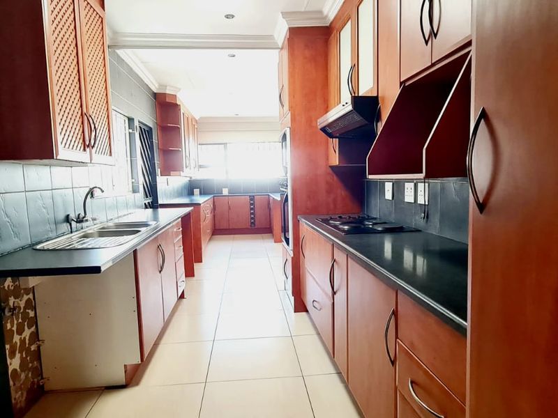 A galley-style kitchen featuring wooden cabinetry, dark countertops, a built-in hob, and tiled finishes, offering a functional layout with ample storage space.