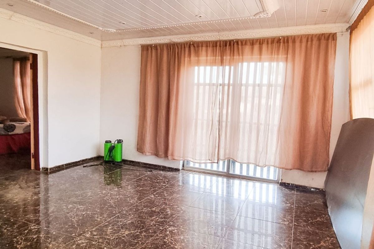 Spacious living area featuring polished dark marble-style floor tiles, a decorative recessed ceiling with integrated lighting, and sliding glass doors leading outdoors.