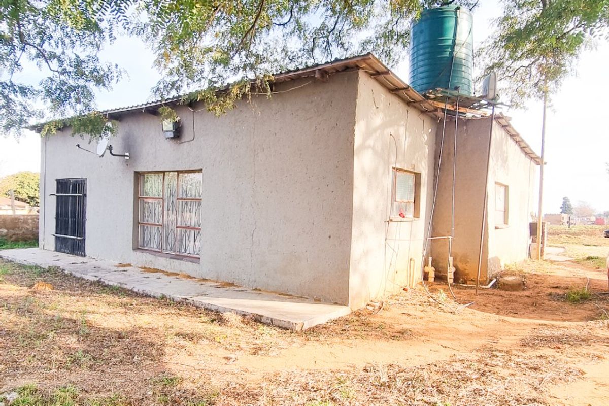 Rear view of a farm dwelling featuring a water storage tank, security gates, and a concrete apron set within a natural landscape.