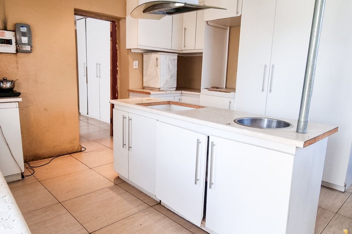 A dated kitchen featuring a central island with a sink, white cabinetry, an extractor fan, and tiled flooring, requiring cosmetic updates.