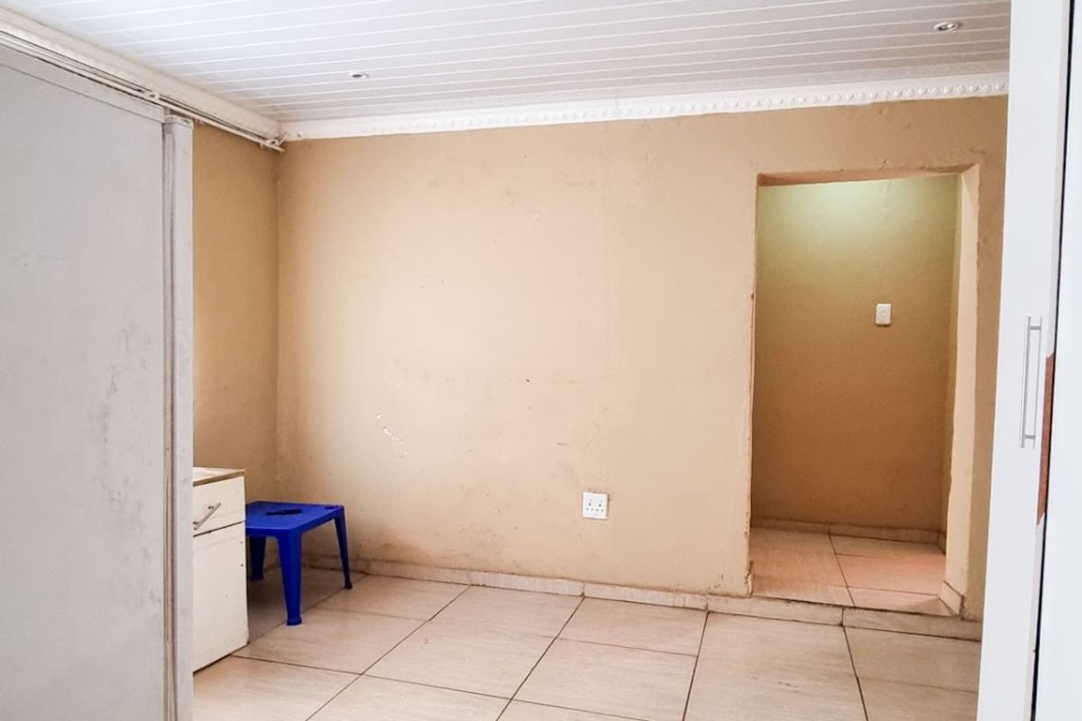 A simple bedroom featuring tiled flooring, a tongue and groove ceiling, and a built-in cupboard, offering a blank canvas for potential updates.
