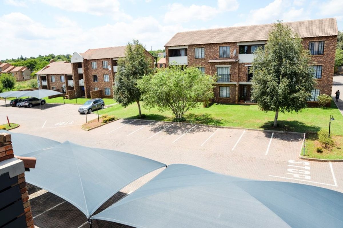Elevated view of a residential complex featuring brick buildings, paved parking bays with shade cloth carports, and well-maintained communal garden areas.