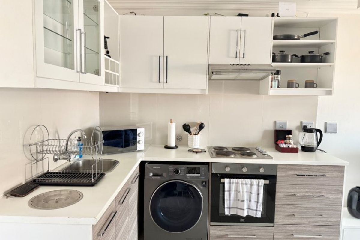 A compact, modern kitchen featuring white upper cabinetry, wood-grain lower cabinets, a built-in oven with hob, and an integrated washing machine.