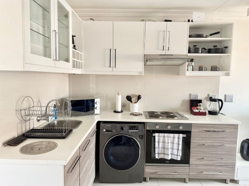 A compact, modern kitchen featuring white upper cabinetry, wood-grain lower cabinets, a built-in oven with hob, and an integrated washing machine.