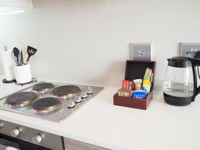 A clean kitchen countertop featuring a built-in electric hob, oven, and glass splashback with integrated electrical fixtures.