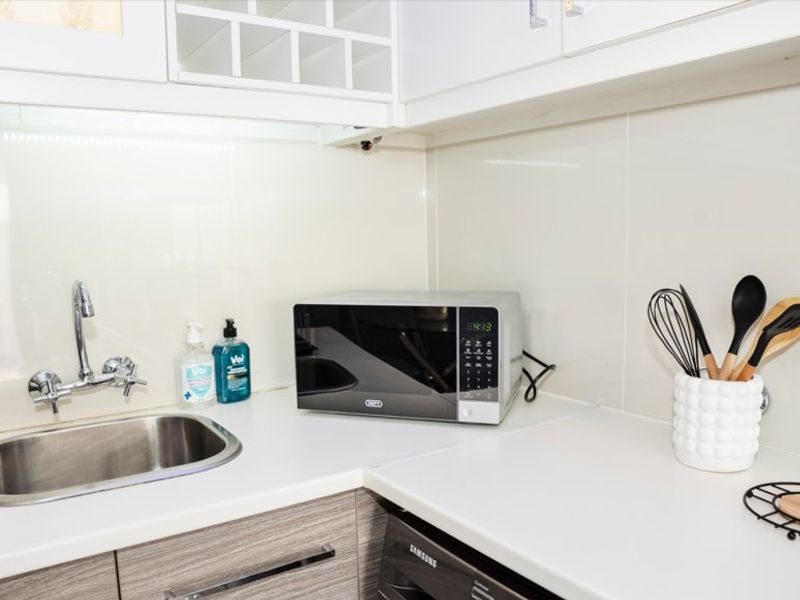 A clean and functional scullery area featuring modern laminate cabinetry, a stainless steel sink, and a sleek glass splashback with integrated under-cabinet lighting.