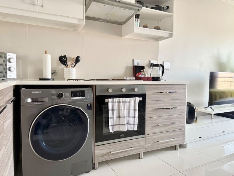 Modern kitchen featuring laminate cabinetry, stone countertops, built-in oven, extractor fan, and an integrated washing machine with sleek tiled flooring.