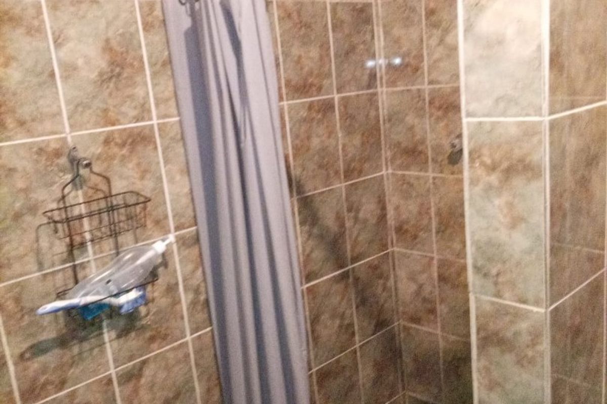 A functional bathroom shower area featuring floor-to-ceiling tiled walls and a standard shower mixer setup.