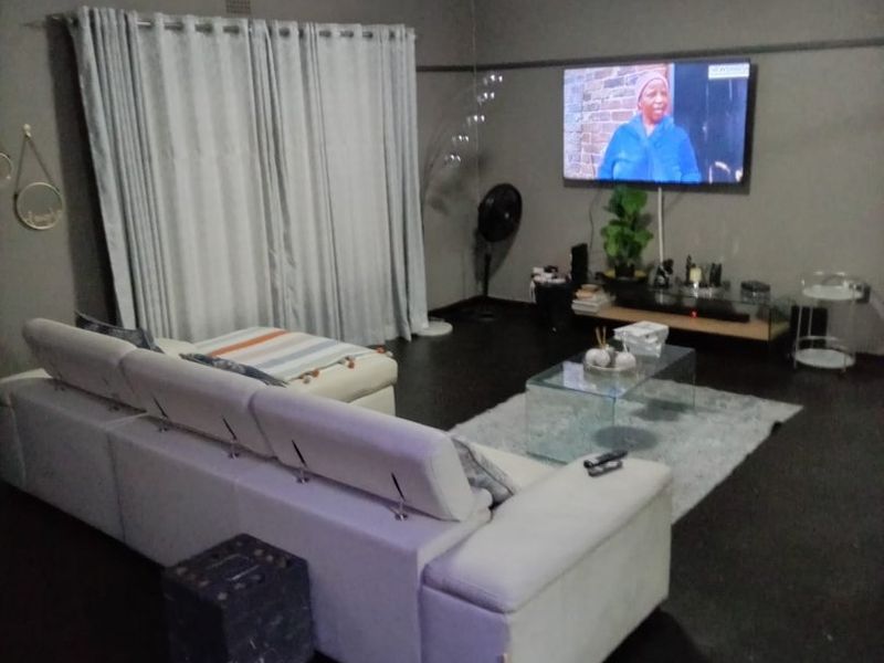A comfortable living room featuring dark flooring, ceiling cornicing, and neutral grey walls, providing a functional and relaxed space for daily living.