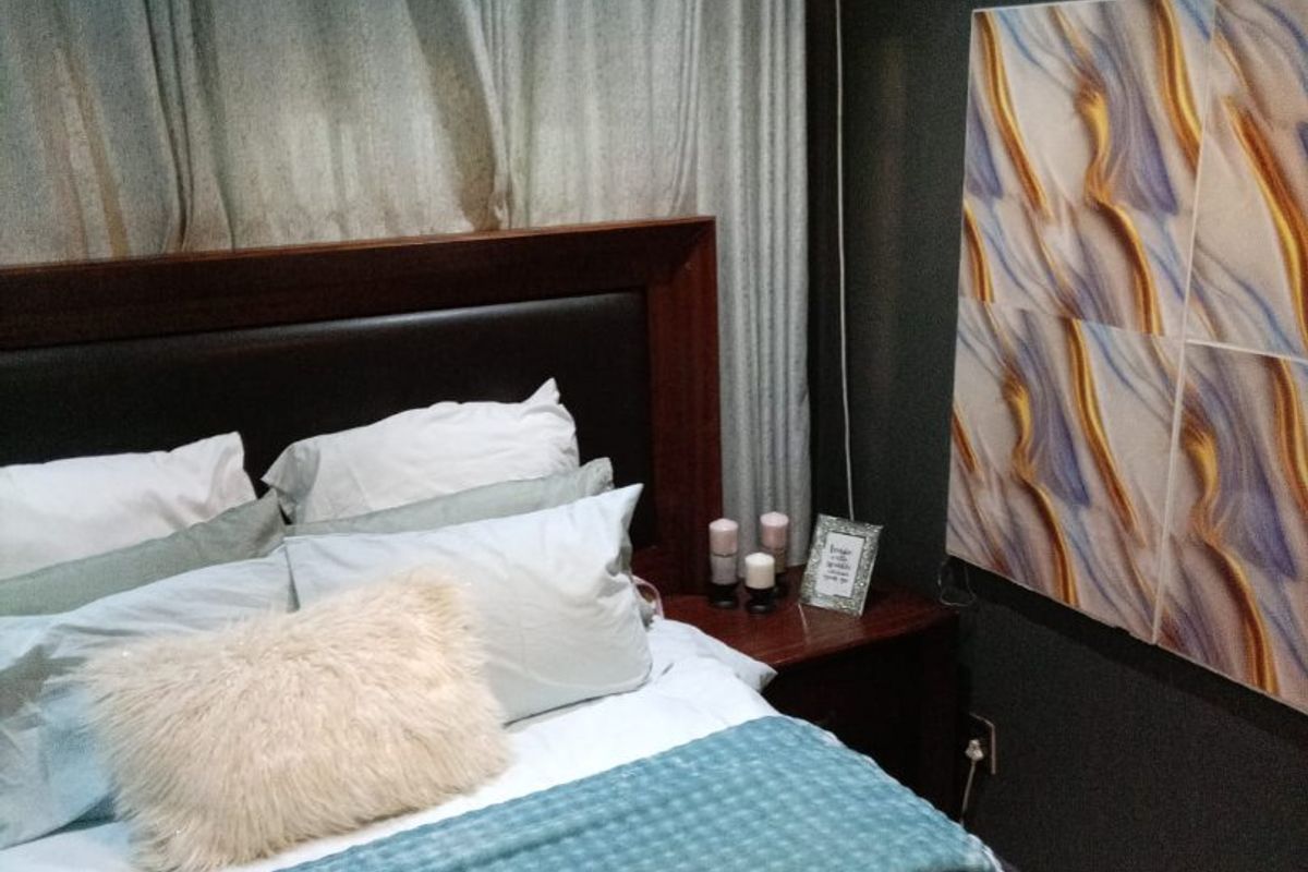A cozy bedroom featuring dark-toned walls, a built-in headboard, and a modern pendant light fixture.