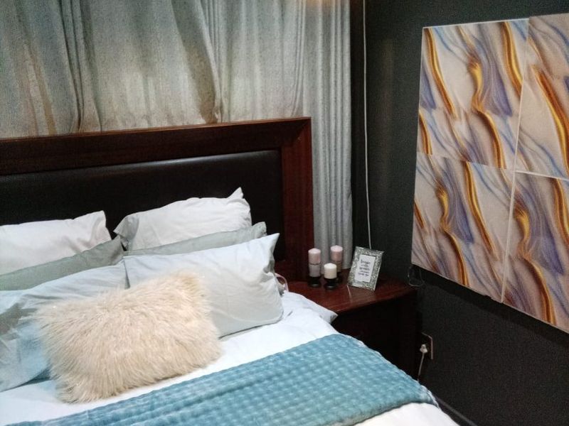 A cozy bedroom featuring dark-toned walls, a built-in headboard, and a modern pendant light fixture.