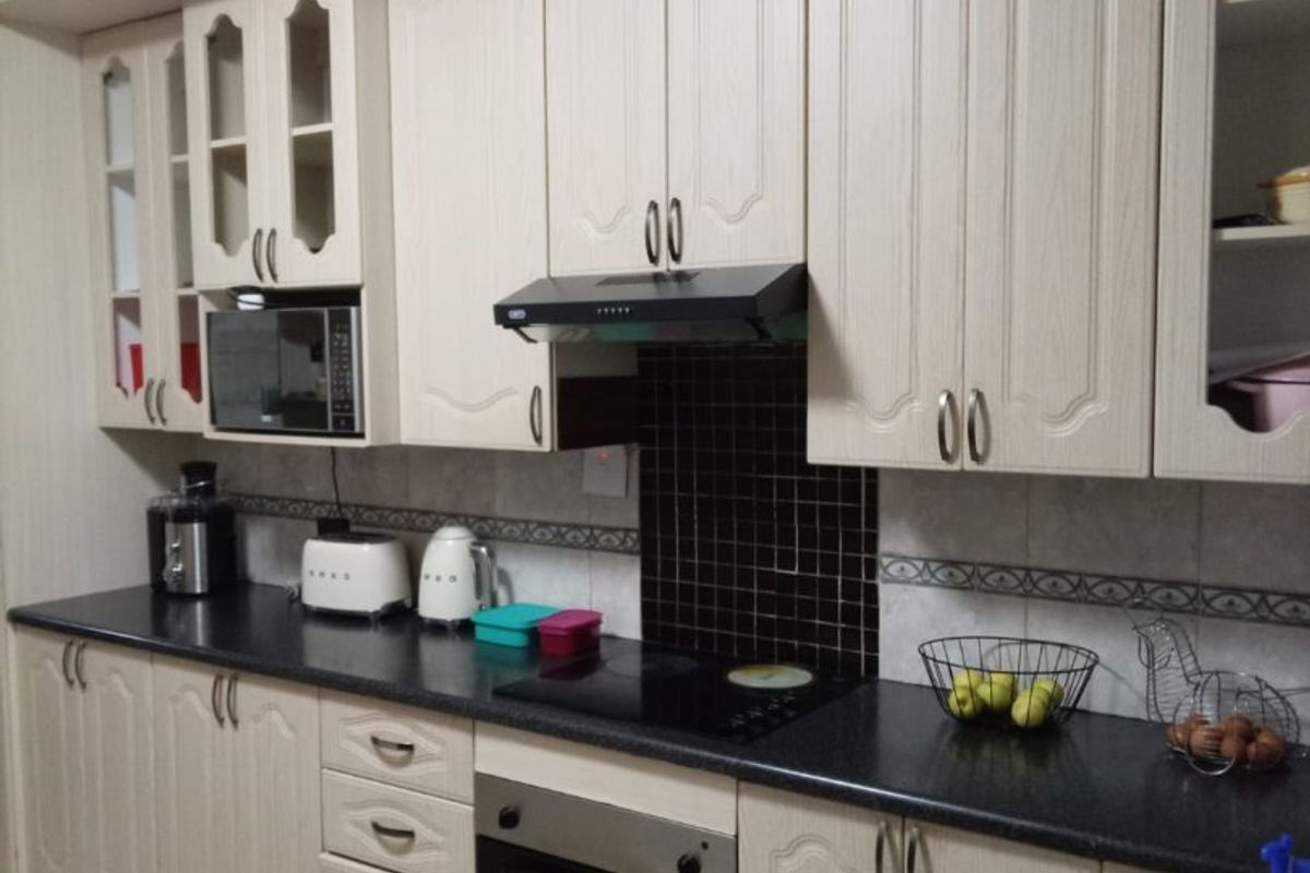 A functional kitchen featuring light wood-grain cabinetry, dark countertops, a built-in oven, and a tiled backsplash with decorative border detailing.