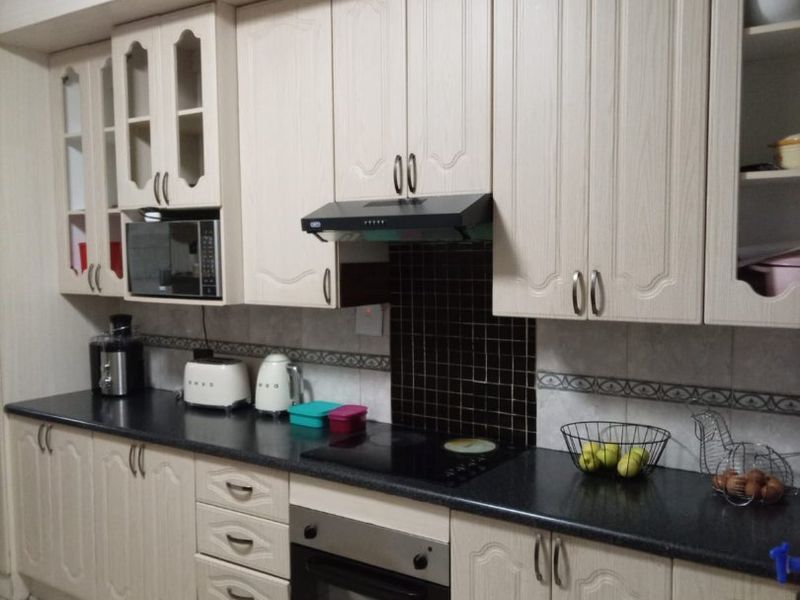A functional kitchen featuring light wood-grain cabinetry, dark countertops, a built-in oven, and a tiled backsplash with decorative border detailing.