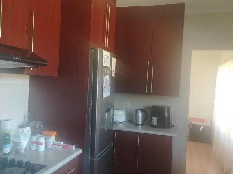 A functional kitchen featuring dark wood-finish cabinetry, laminate countertops, built-in oven, and gas hob, with tiled flooring and direct access to an adjacent living area.