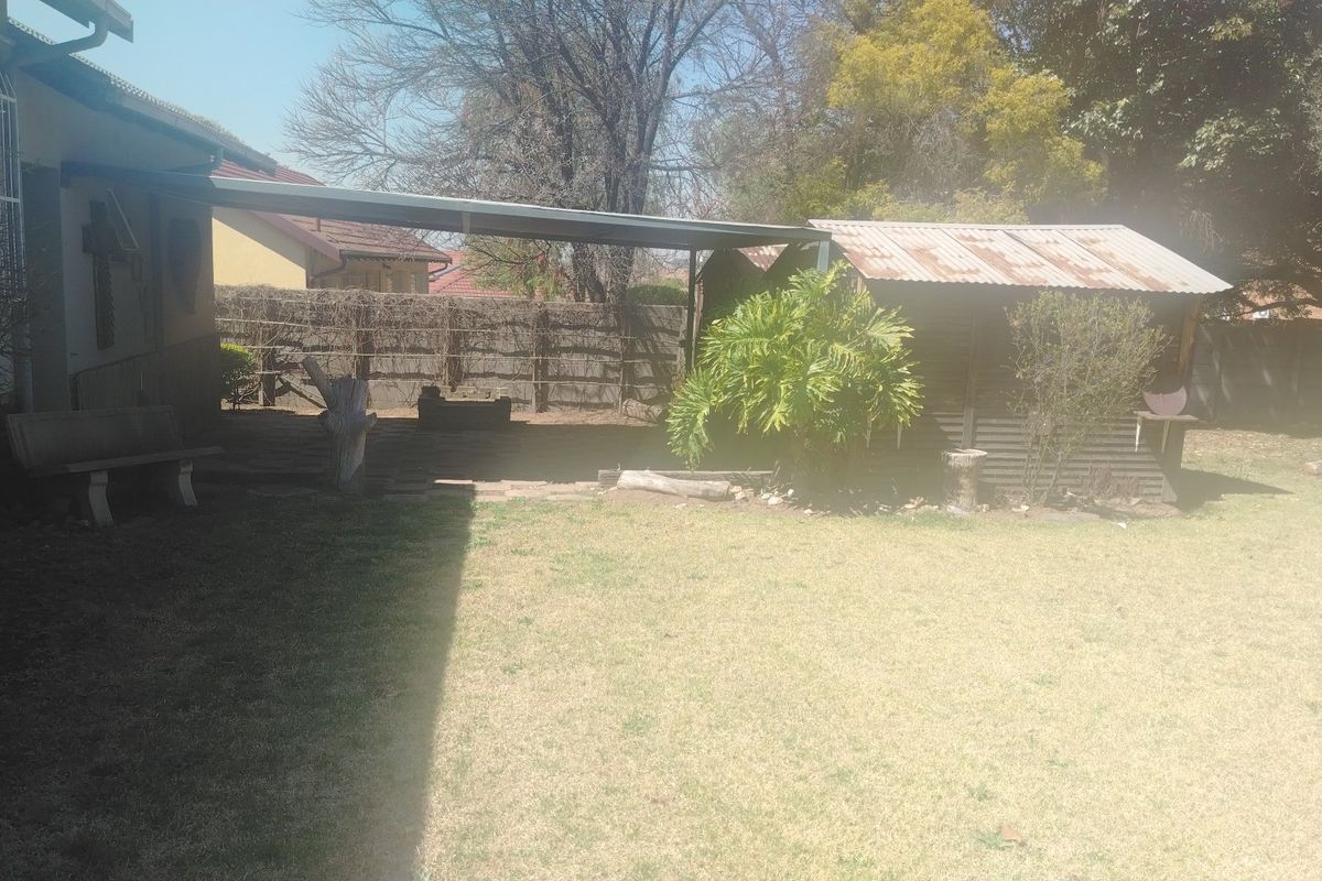 A rear garden area featuring a covered patio space and a detached corrugated metal storage shed set within a lawned yard.
