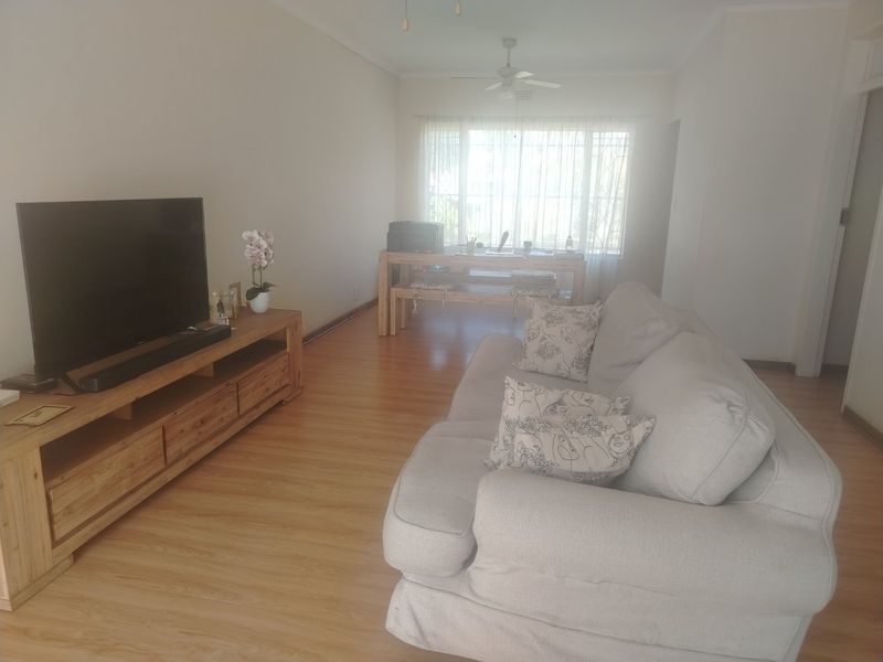 A spacious living room featuring laminate flooring and a ceiling fan, with natural light entering through a large window.