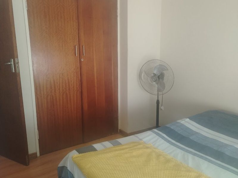 A bedroom featuring laminate flooring and a built-in wooden wardrobe with overhead storage compartments.