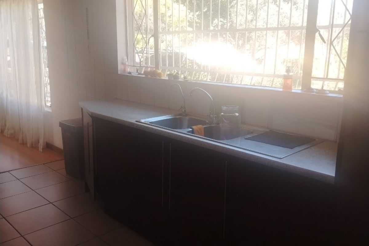 A functional kitchen area featuring dark cabinetry, a stainless steel sink, and tiled flooring, illuminated by a large window with security bars.