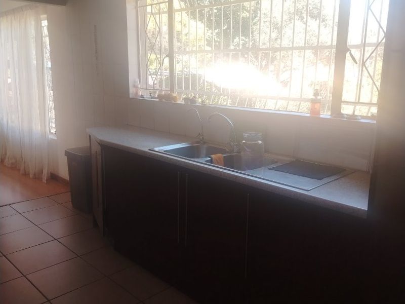 A functional kitchen area featuring dark cabinetry, a stainless steel sink, and tiled flooring, illuminated by a large window with security bars.