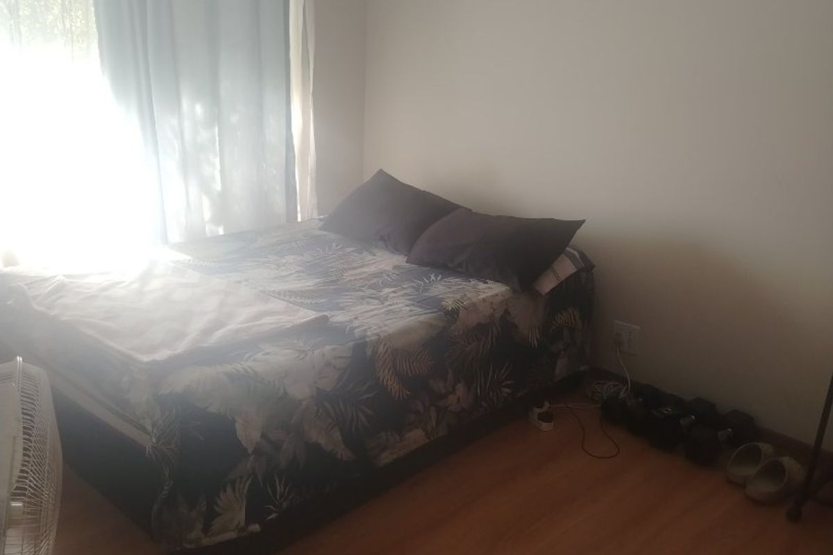 A standard bedroom featuring laminate flooring and a window with curtain rails, providing a functional sleeping space.