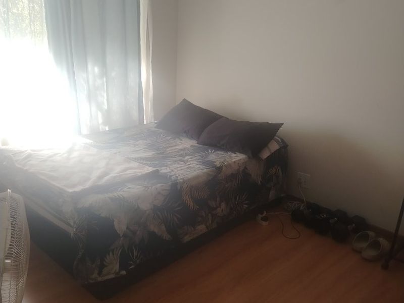 A standard bedroom featuring laminate flooring and a window with curtain rails, providing a functional sleeping space.