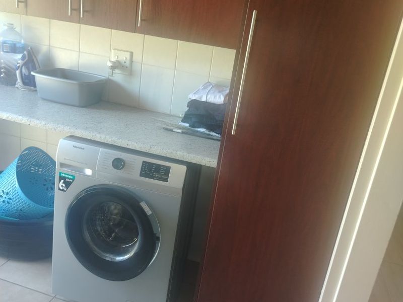 A functional laundry area featuring dark wood-finish cabinetry, a stone-look laminate countertop, and tiled flooring with space for a front-loading washing machine.