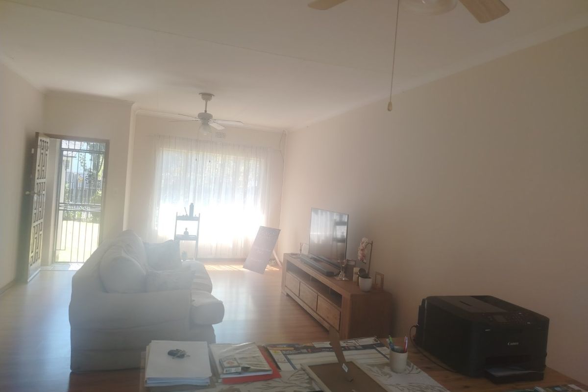 A spacious living room featuring laminate flooring, ceiling fans, and direct access to the exterior through a security gate.
